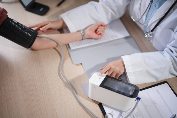 Mujeres psicólogas asiáticas que usan esfigmomanómetro digital para controlar la presión arterial y la frecuencia cardíaca de pacientes mujeres mientras dan consejos sobre medicina y terapia de salud mental en la clínica. - Foto, Imagen
