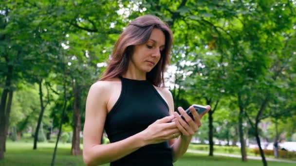 Actieve mooie yogi vrouw tijdens een wandeling in het park voor of na de training staat met een fitness mat met smartphone in haar handen - Video