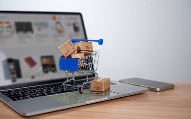 Skrzynki na zakupy i produkty umieszczone na laptopie reprezentują koncepcję zakupów online, stronę internetową, e-commerce, platformę marketplace, technologię, transport, logistykę i koncepcję płatności online. - Zdjęcie, obraz