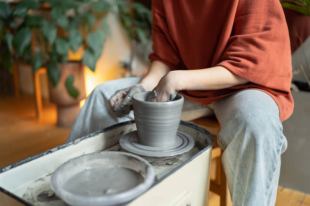Руки майстра кераміки працюють, сидячи в затишній майстерні, використовуючи гончарне колесо для виготовлення глиняного посуду. Процес створення посуду ручної роботи в художній студії для творчих підприємців і ремісників
  - Фото, зображення
