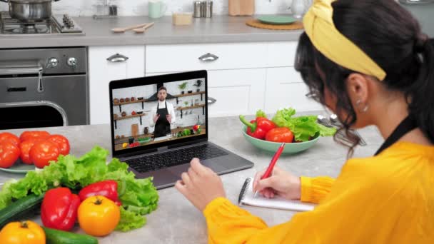 Žena v domácí kuchyni studovna hodinky vzdálené kulinářské webinář poslouchat kuchař učitel, píše v notebooku. Man food blogger na obrazovce počítače říká učí hospodyňky on-line video hovor webcam chat laptop - Záběry, video