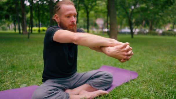 όμορφος γενειοφόρος άνδρας διαλογίζεται στο πάρκο πρακτική γιόγκα κάνει τέντωμα και ασκήσεις διαφορετικές μυϊκές ομάδες - Πλάνα, βίντεο