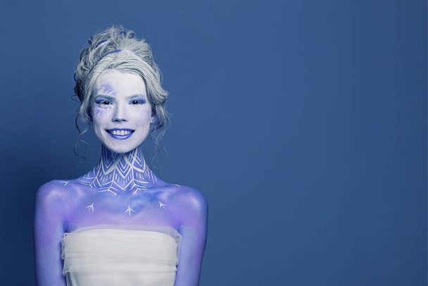 Engraçado inverno rainha mulher atriz com maquiagem palco e sorriso bonito no fundo bandeira azul. Halloween, carnaval, performance e conceito de teatro - Foto, Imagem