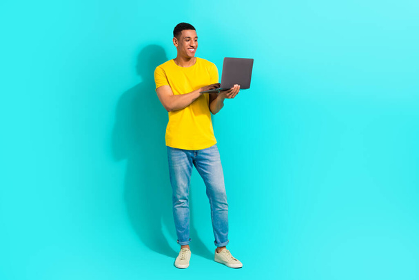 Full length photo of cool cheerful guy wear yellow t-shirt working modern device isolated teal color background. - Foto, Imagen