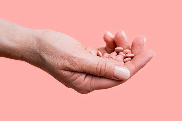 Close-up van vele roze pillen in de hand van de vrouw op roze achtergrond. Medisch concept van medische behandeling, vitaminen, supplementen, anticonceptiepillen of vrouwelijke drugsverslaving. Selectieve focus. - Foto, afbeelding
