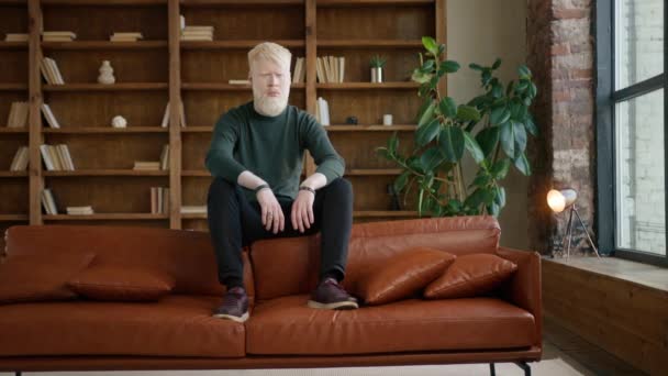 Biznesmen Albinos siedzi na kanapie w biurze. Zwykły człowiek smuci się samotnie. Przygnębiony facet zamyka oczy. Mężczyzna model pozowanie w nowoczesnym wnętrzu poddasza. Młody człowiek myśli o kryzysie finansowym  - Materiał filmowy, wideo