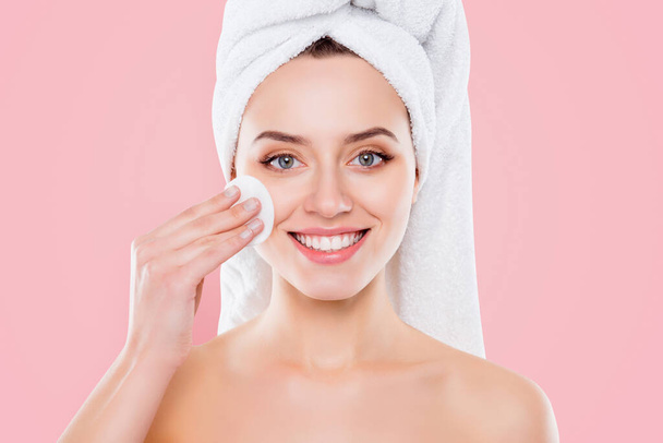 Close up of attractive charming girl with towel on her head, isolated on white background, touching her cheek with a white sponge, looking at camera. - 写真・画像