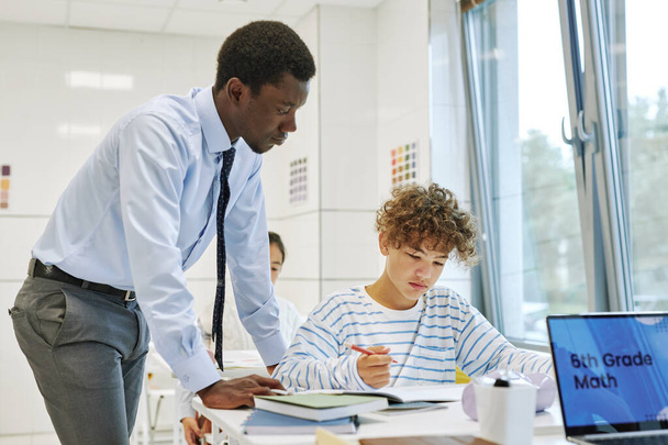 Side view portrait of young black teacher helping boy in school classroom - Photo, Image