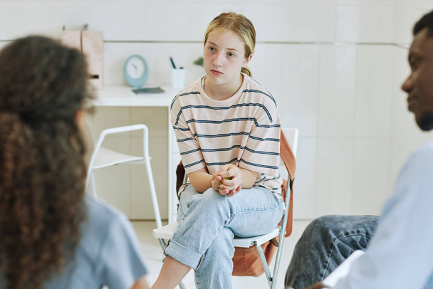 Retrato de una joven adolescente en círculo de apoyo escuchando a niños compartiendo historia en terapia de salud mental - Foto, imagen