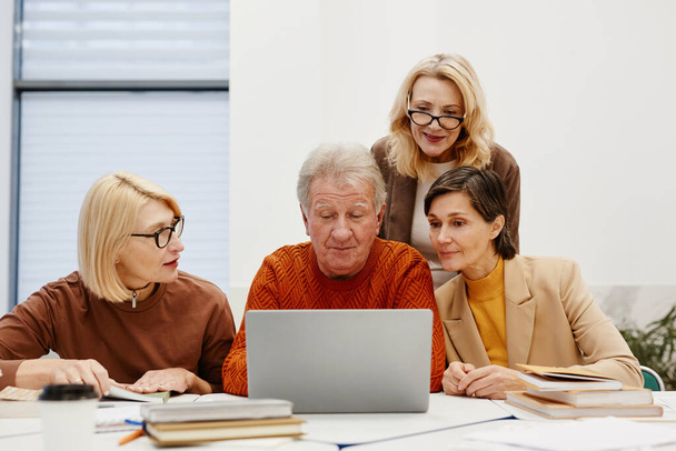 Ομάδα ηλικιωμένων που μαθαίνουν να χρησιμοποιούν το φορητό υπολογιστή μαζί, ενώ κάθονται στο γραφείο κατά τη διάρκεια της εκπαιδευτικής κατάρτισης - Φωτογραφία, εικόνα