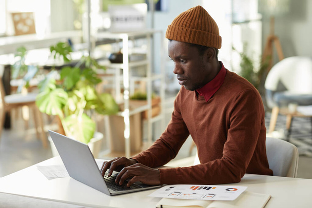 Retrato de vista lateral del joven negro que trabaja con el ordenador portátil en el lugar de trabajo de la oficina y el análisis de datos de marketing, espacio de copia - Foto, Imagen