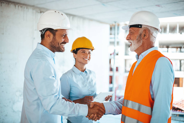 Woman architect or engineer looking at male colleagues handshaking at construction site  - Photo, image