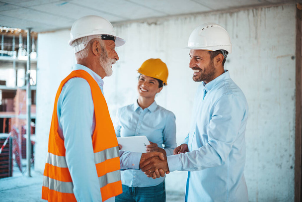 Arquitecta o ingeniera mirando a colegas masculinos estrechando las manos en el sitio de construcción  - Foto, imagen