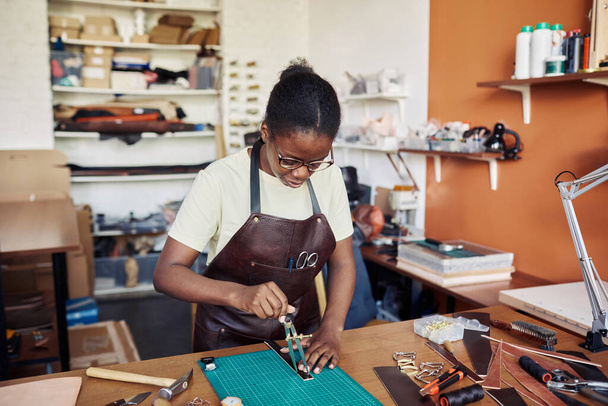 Retrato de mujer artesana negra midiendo pieza de cuero en taller de cuero y creando diseños hechos a mano - Foto, imagen