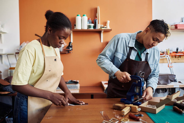 Portrait latéral de deux jeunes femmes multiethniques travaillant avec du cuir en atelier et créant des pièces faites main - Photo, image