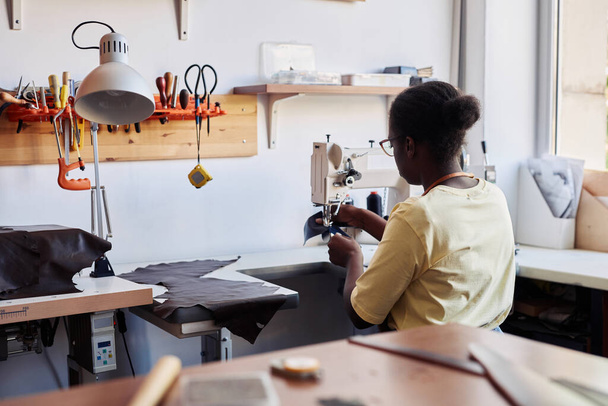 Обратный вид молодой женщины с помощью швейной машинки и создание ручной кожаной сумки в мастерской, копировальное пространство - Фото, изображение