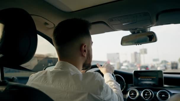 δείτε πίσω έναν άνθρωπο ένας επιχειρηματίας οδηγεί ένα πολυτελές αυτοκίνητο γύρω από την πόλη ένα μαύρο δέρμα εσωτερική πλοήγηση οθόνη μποτιλιάρισμα - Πλάνα, βίντεο