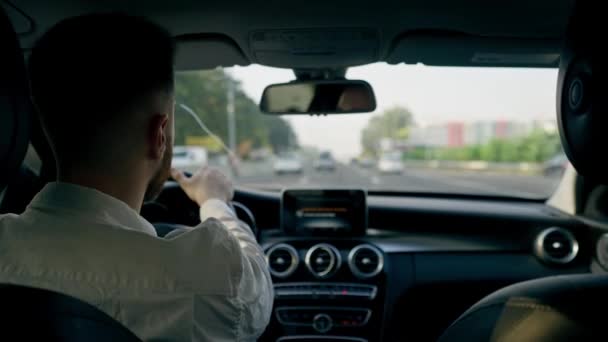 δείτε πίσω έναν άνθρωπο ένας επιχειρηματίας οδηγεί ένα πολυτελές αυτοκίνητο γύρω από την πόλη ένα μαύρο δέρμα εσωτερική πλοήγηση οθόνη μποτιλιάρισμα - Πλάνα, βίντεο