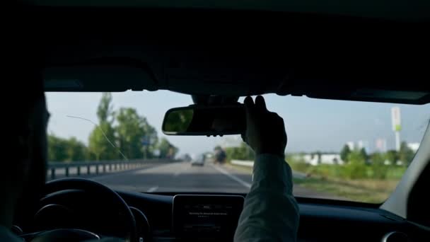 ο οδηγός πίσω από το τιμόνι ενός πολυτελούς αυτοκινήτου οδηγεί κατά μήκος της εθνικής οδού και κοιτάζει στον καθρέφτη - Πλάνα, βίντεο