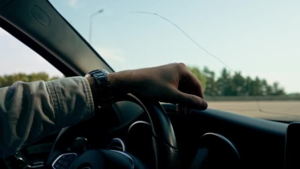 市内の高級車の運転の内部の車輪の後ろの男性の運転者の腕時計との手のクローズアップ - 映像、動画
