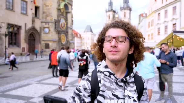 Praga, Czechy, 4.2023 sierpnia. Młody mężczyzna kaukaski robi sobie selfie z jednym z najpiękniejszych i kultowych widoków - starym rynkiem z zegarem astronomicznym i kościołem w tle - Materiał filmowy, wideo