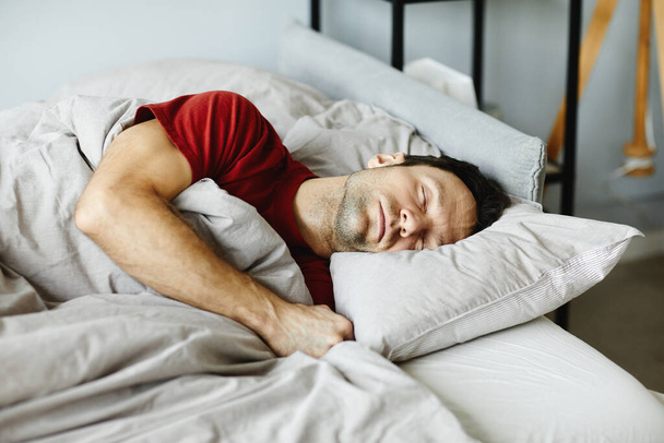 成熟した男は毛布の下の枕に横たわり,寝室のベッドで寝ている - 写真・画像