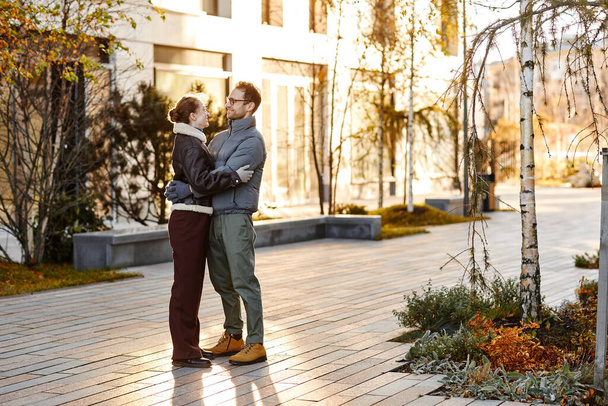 Giovane coppia che si abbraccia in piedi sulla strada e godersi la loro passeggiata in autunno giorno - Foto, immagini