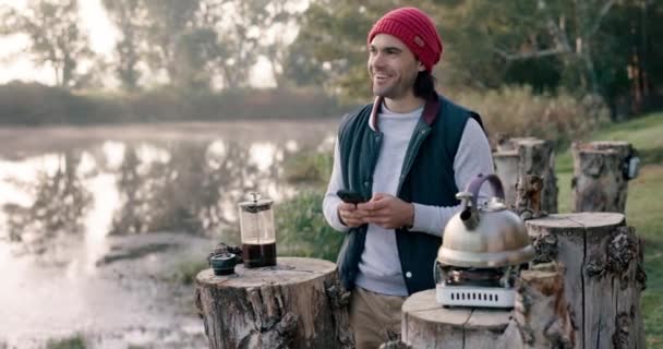 Camping, nature and man with coffee and phone in nature on outdoor holiday, vacation and adventure. Campsite, travel and male person online for social media, internet and chat on mountain in morning. - Footage, Video