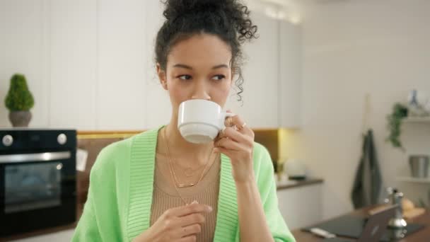 Жаждущая улыбка 20-х годов многорасовая женщина начинает новый день с чашки ароматного кофе, стоящего в одиночестве в современном кухонном интерьере. Разнообразная модель питья из белой чашки крупным планом, люди ведут образ жизни 4K - Кадры, видео