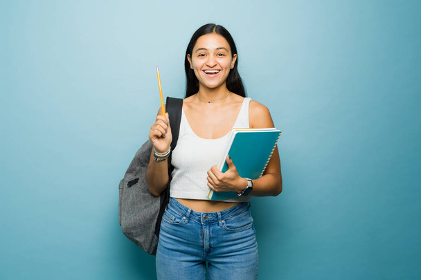 Έξυπνη χαρούμενη νεαρή γυναίκα και φοιτήτρια έτοιμη να κρατήσει σημειώσεις στην τάξη ενώ πηγαίνει στο πανεπιστήμιο κουβαλώντας βιβλία και ένα σακίδιο πλάτης - Φωτογραφία, εικόνα