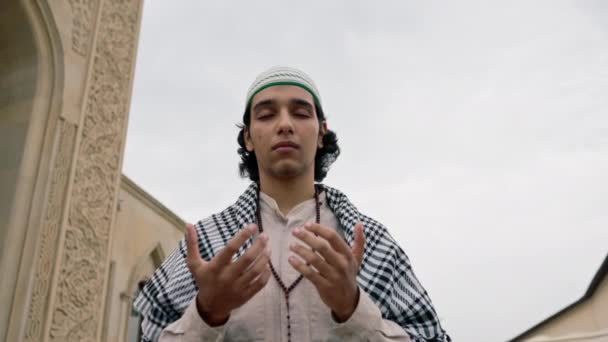 Un ragazzo di aspetto arabo in abiti nazionali con un rosario intorno al collo prega nel cortile della moschea - Filmati, video