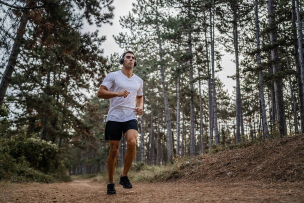 un homme jeune athlète homme caucasien courir à travers les bois dans la nature jogging en plein air en automne ou en été jour sport fitness et loisirs mode de vie sain concept personnes réelles copier l'espace - Photo, image