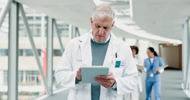 Doctor, senior man and tablet for thinking, reading results analysis and healthcare app in clinic corridor. Male medic, touchscreen or notes in hospital hallway for info, review or medical research. - Footage, Video