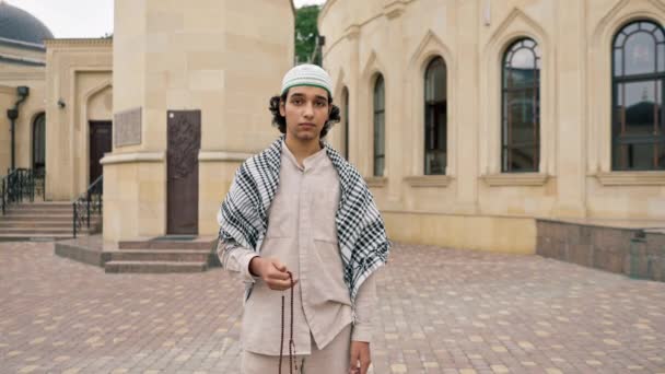 Un chico de apariencia árabe con ropas nacionales con un rosario en la mano reza y adora a Allah en la mezquita - Metraje, vídeo