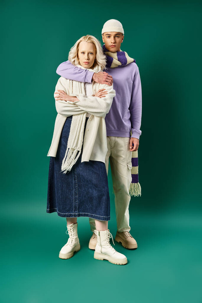 full length of tall and stylish man hugging blonde woman in winter attire on turquoise backdrop - Photo, Image