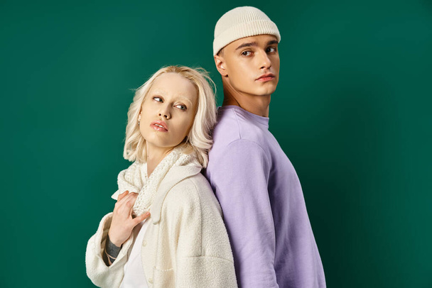 lange man in hoed en winter kleding poseren rug aan rug met blonde vrouw op turquoise achtergrond - Foto, afbeelding
