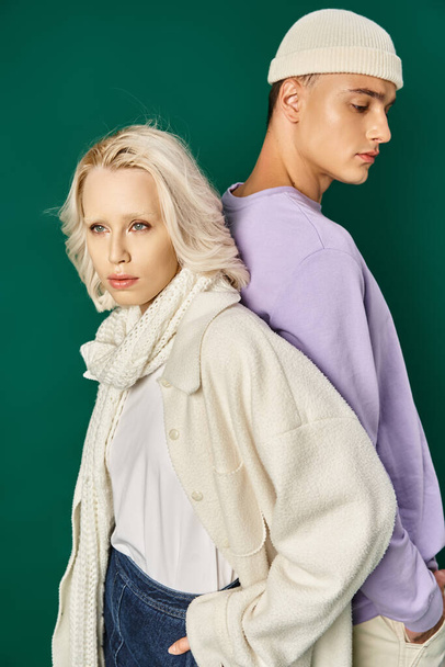blondýny žena v zimním oblečení pózování s rukou v kapse a zády k sobě s vysokým mužem na tyrkysové - Fotografie, Obrázek