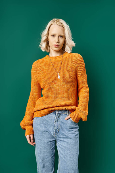 pretty blonde woman in mustard yellow sweater and jeans posing with hand in pocket on turquoise - Photo, Image
