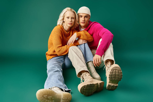 セーターでトレンディなカップル, ブロンドの女性と男は,ターコイズの背景に一緒に座ってビーニー - 写真・画像