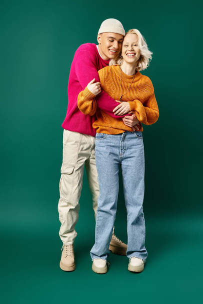 ζευγάρι σε χειμωνιάτικα πουλόβερ, άντρας σε σκούφο αγκαλιάζει χαρούμενη φιλενάδα σε τυρκουάζ, χειμωνιάτικη μόδα - Φωτογραφία, εικόνα