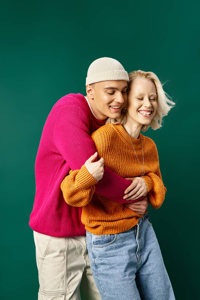 para w stroju zimowym, mężczyzna w czapce obejmujący szczęśliwą dziewczynę na turkusowej, zimowej modzie - Zdjęcie, obraz