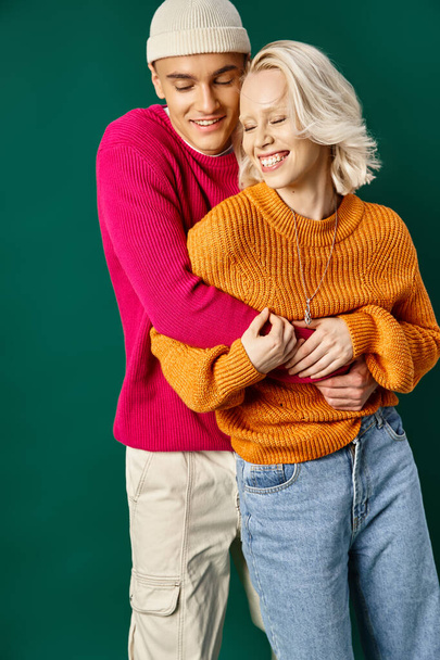 gelukkig paar in de winter kleding hebben plezier, man in beanie omarmen vriendin op turquoise achtergrond - Foto, afbeelding