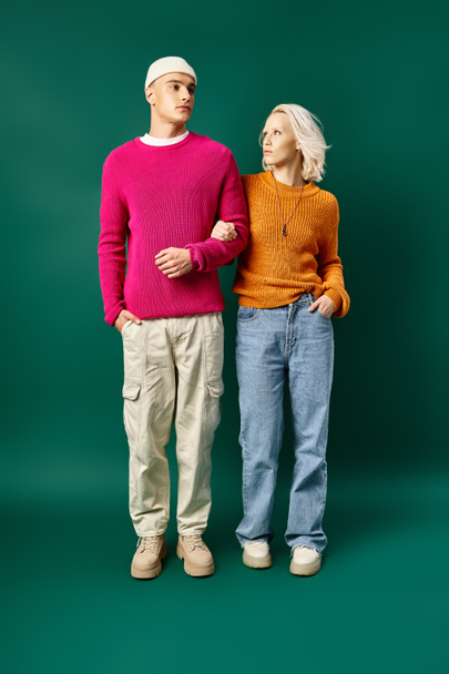 fashionable man and woman in winter outfits posing with hands in pockets on turquoise background - Photo, Image