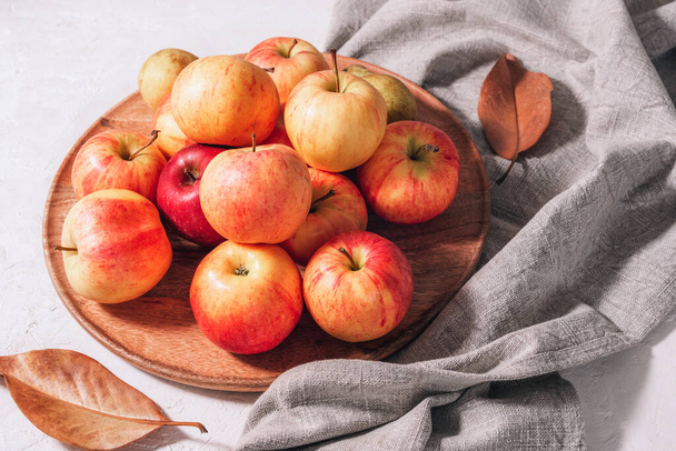 Manzanas frescas maduras en bandeja de madera, hojas de otoño y servilleta gris sobre mesa blanca. Cosecha otoñal, concepto de Acción de Gracias. Vista superior. - Foto, imagen