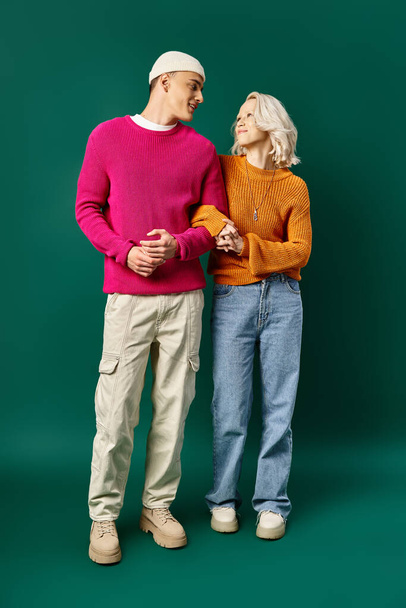 happy couple in winter sweaters standing hand to hand on turquoise background, young woman and man - Photo, Image