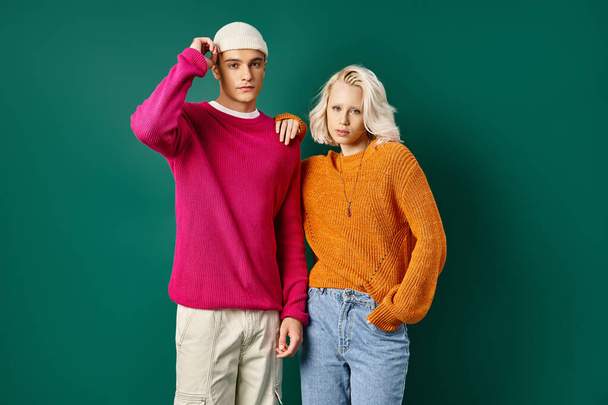 fashionable man and blonde woman in winter outfits posing together on turquoise background - Photo, Image