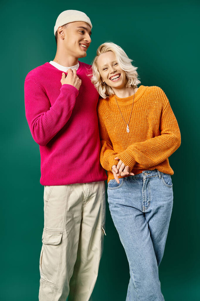 веселая молодая пара в зимних свитерах смеется и смотрит в камеру на бирюзовом фоне - Фото, изображение