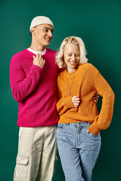 cheerful young couple in winter attire laughing and standing together on turquoise background - Photo, Image