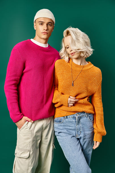 jong blond vrouw poseren met knappe vriend in trui op turquoise achtergrond, jong stel - Foto, afbeelding
