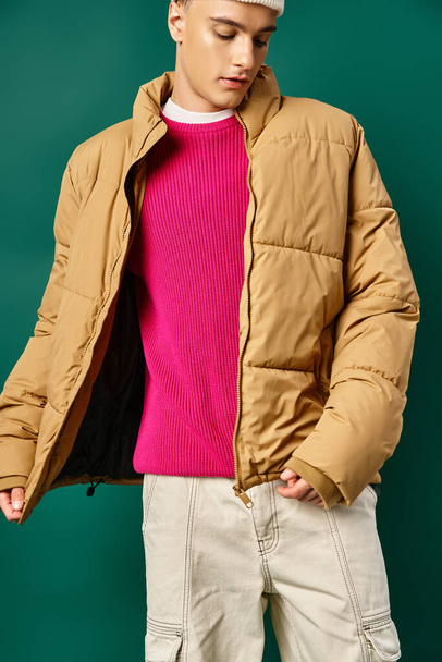 jonge man in muts en winter kogelvrij vest poseren op turquoise achtergrond, winter trends - Foto, afbeelding